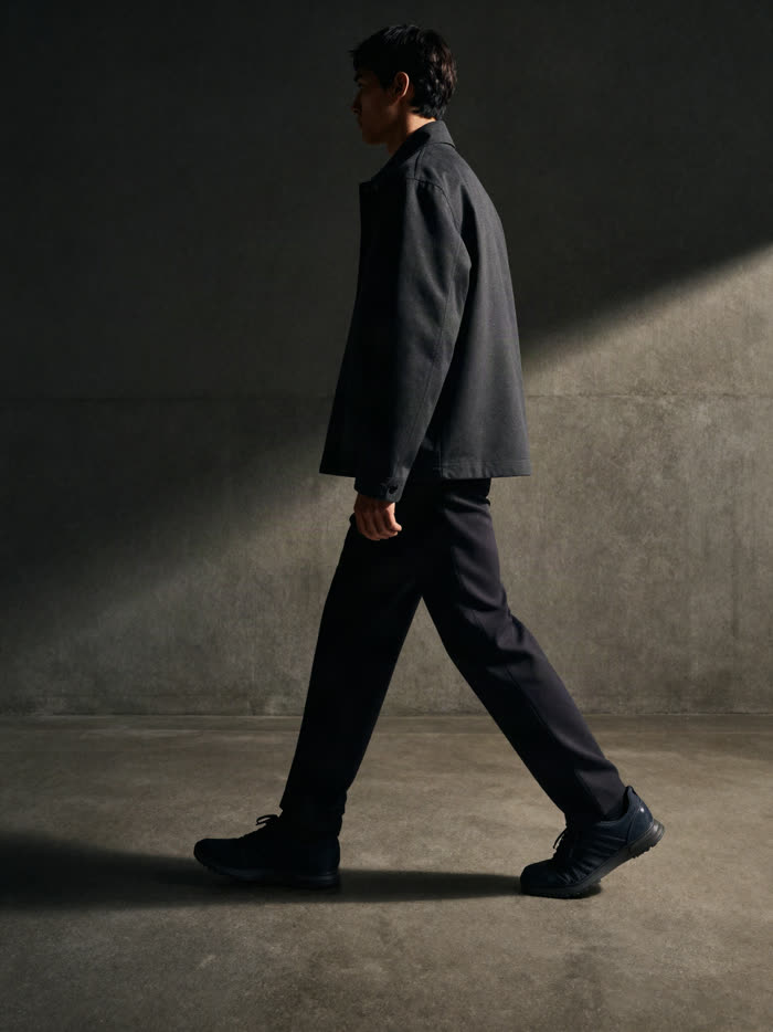 A man mid stride in dark trousers and dark sneakers