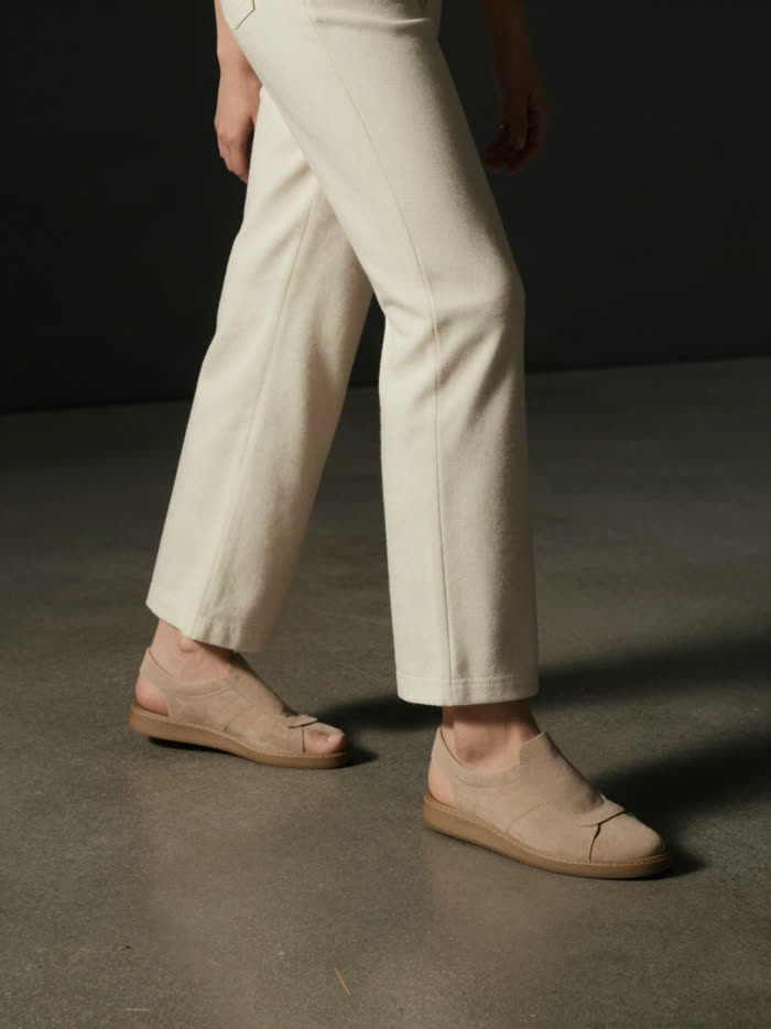 A woman mid step in cream trousers and sand sneakers